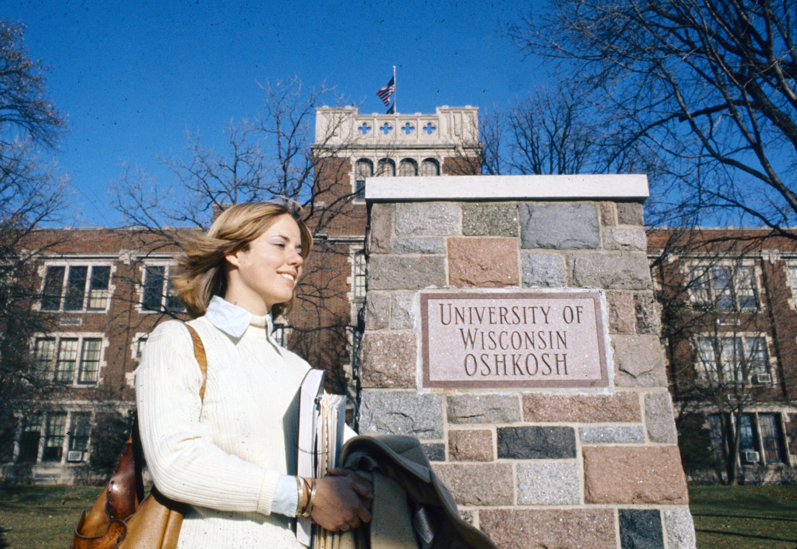 Female student walking past the granite UW-Oshkosh sign in 1930.